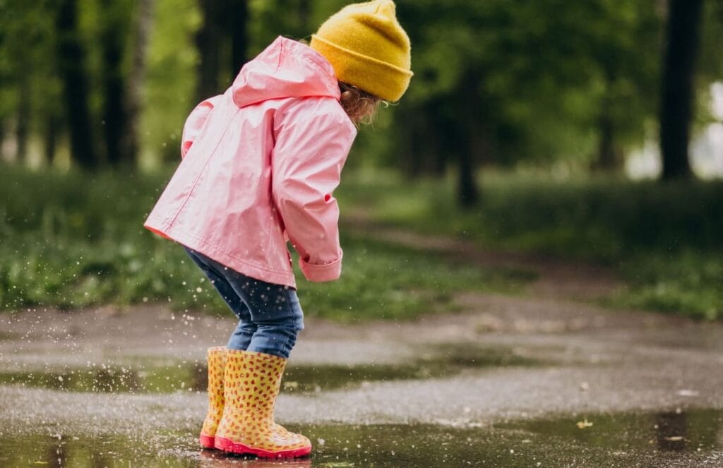 Flicka som leker i en vattenpöl under en regnig dag.